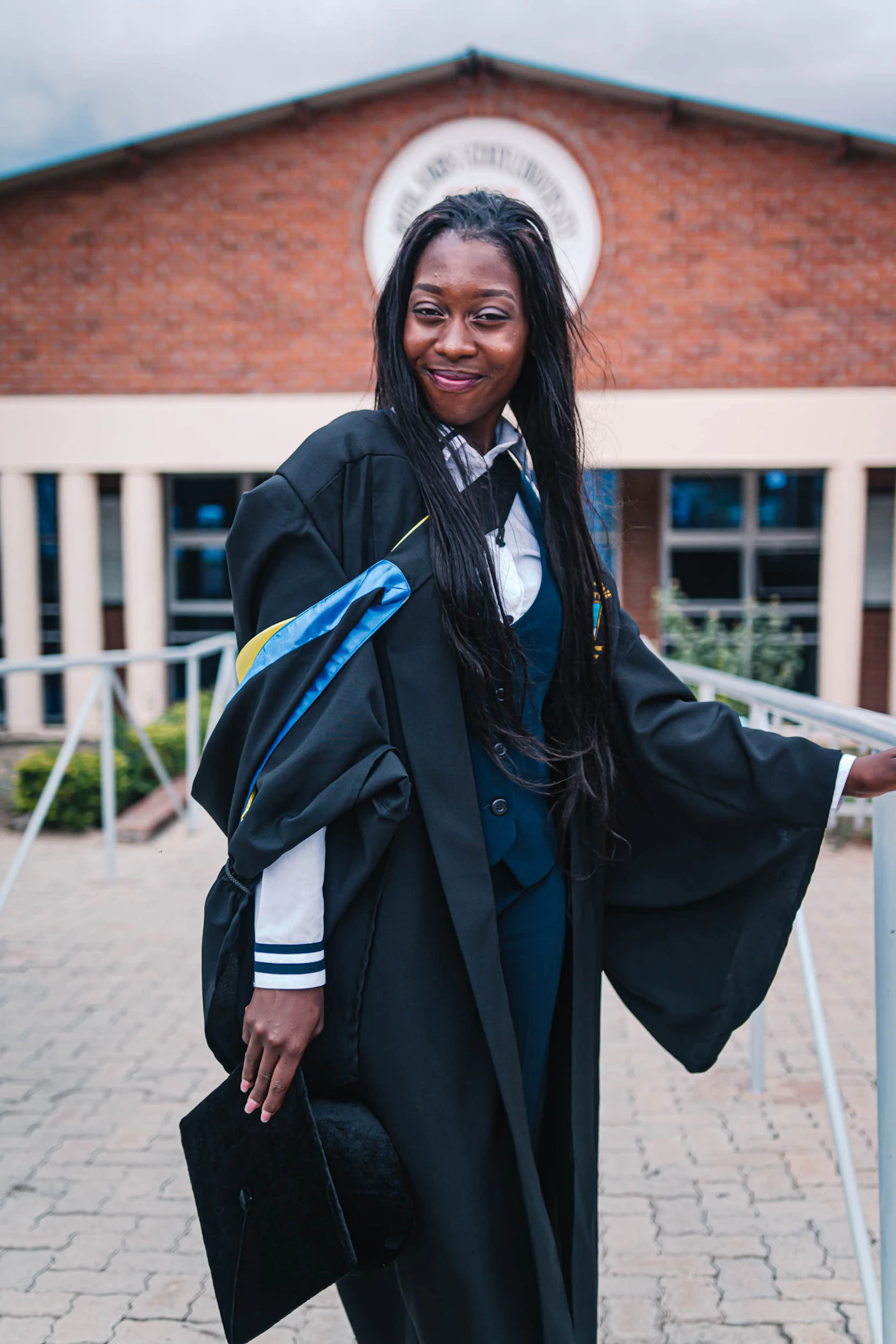 A graduate in cap and gown celebrating outside a university building