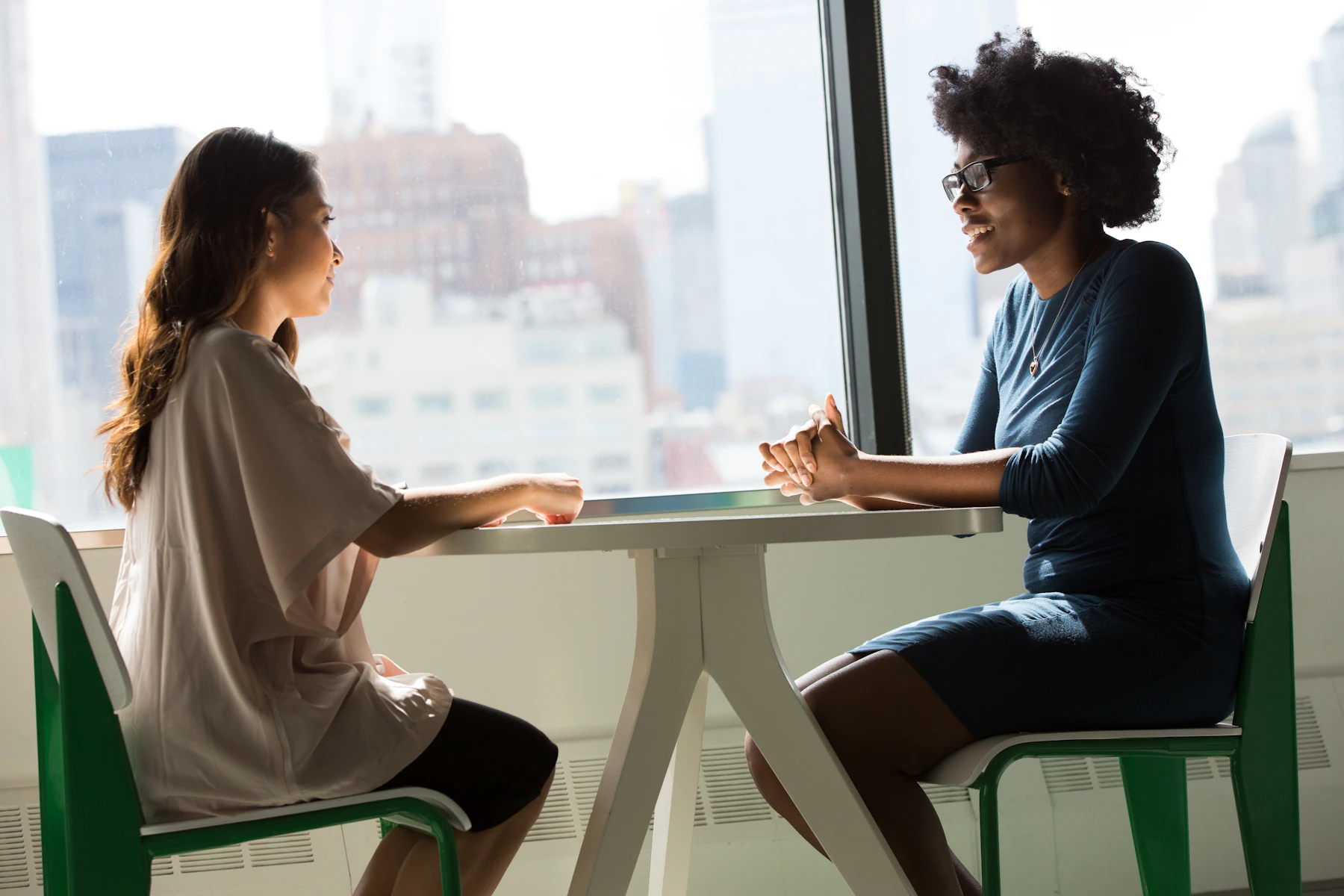 Two women talking across a table in a bright office